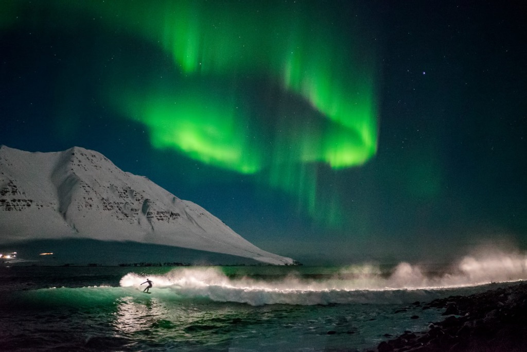 Foto von Chris Burkard zeigt einen Surfer auf einer Welle vor Nordlichtern in Island 